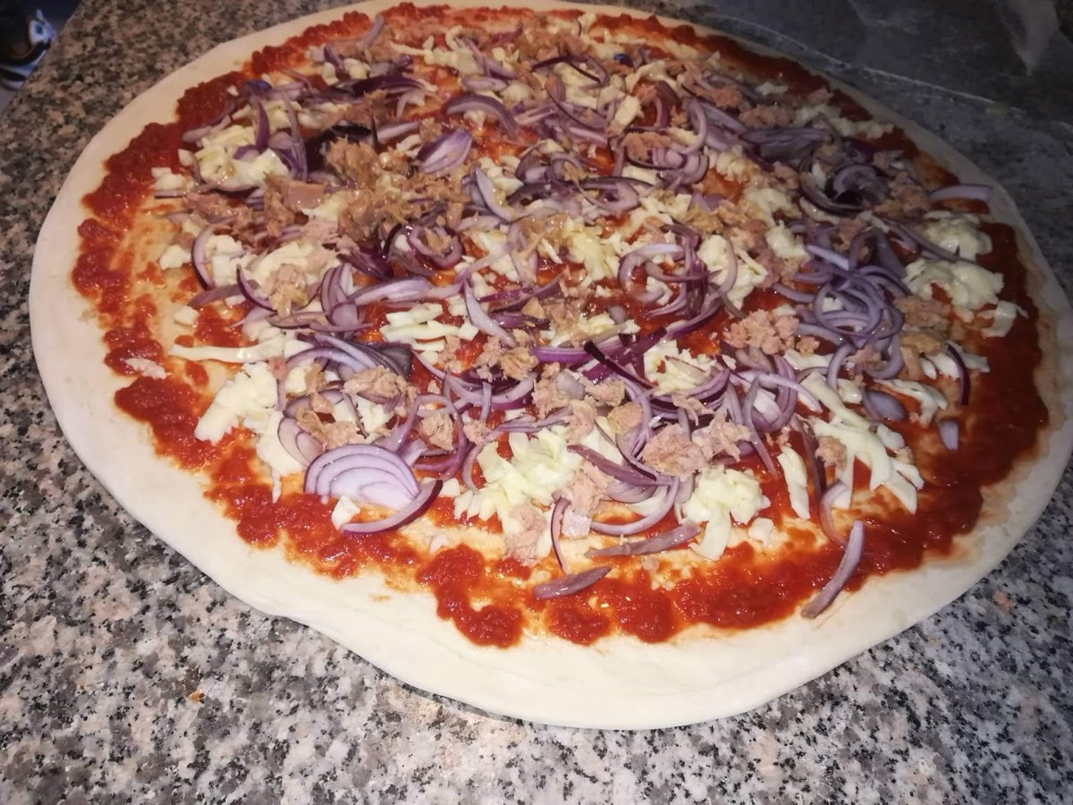 Pizza con tonno, cipolla rossa e mozzarella pronta per il forno a legna